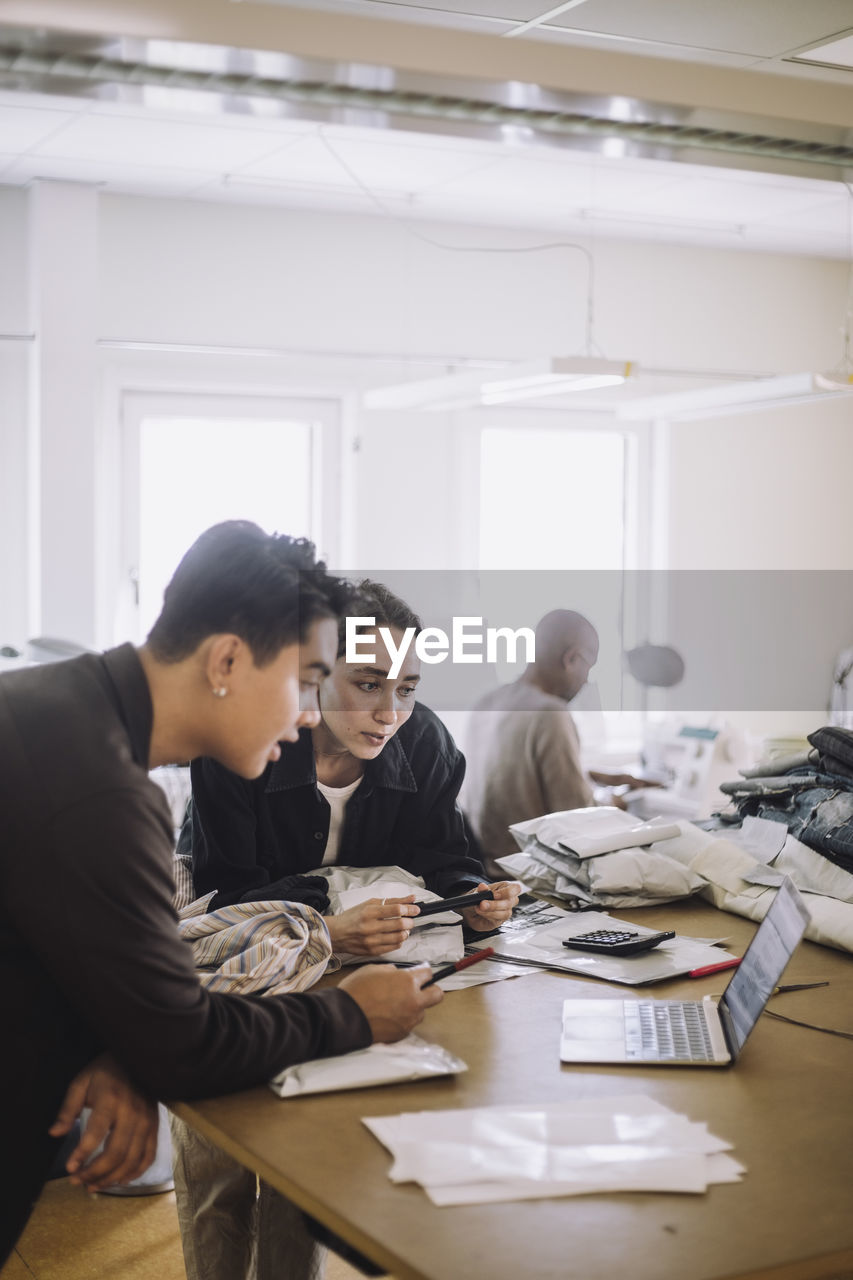 Male and female design professional watching laptop while leaning on workbench at workshop