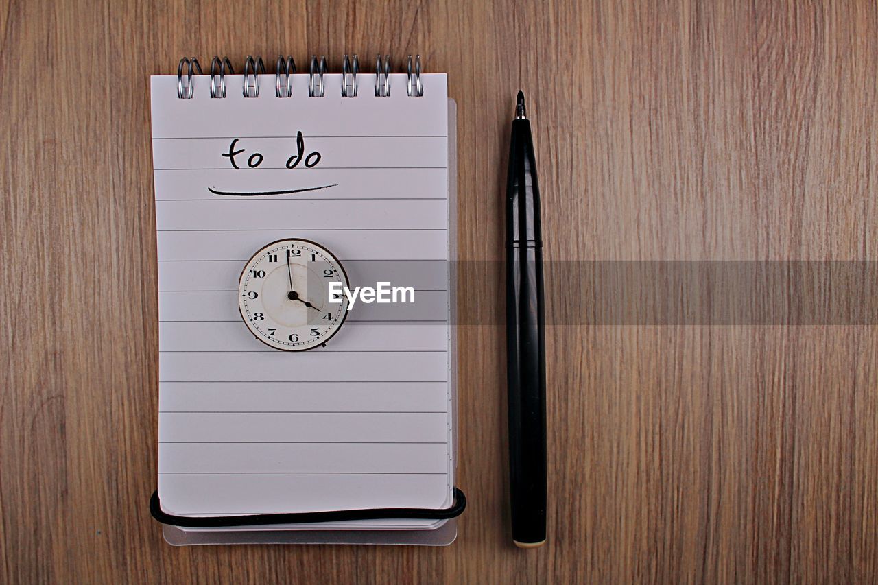 Directly above shot of clock with note pad on wooden table