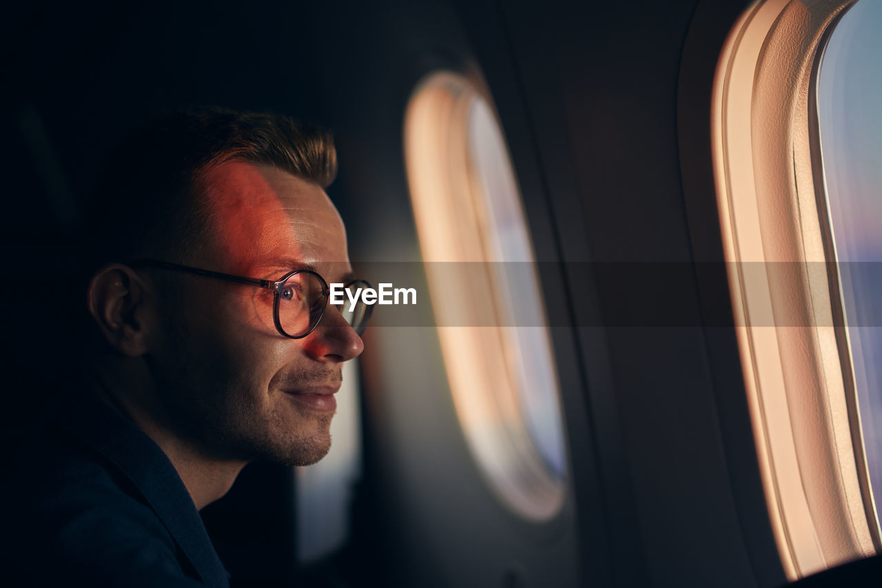 Man with eyeglasses traveling by airplane. passenger looking through window during flight at sunset.