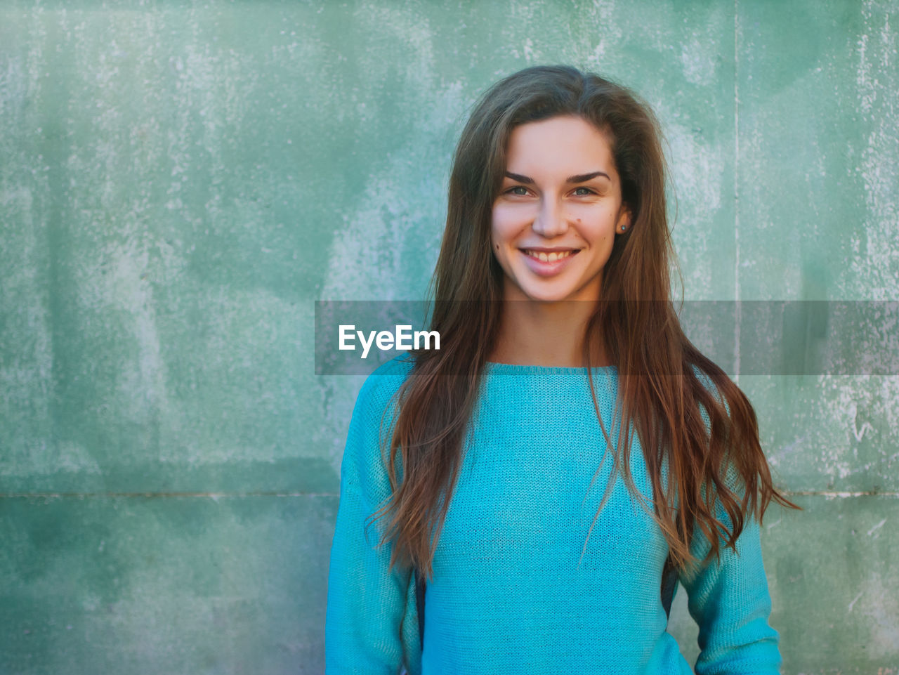 Portrait of smiling young woman standing against wall