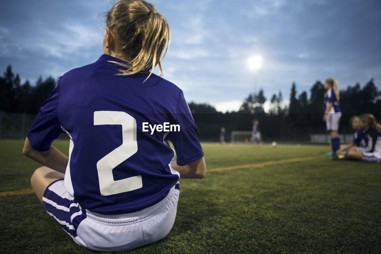 Rear view of girl sitting on field against sky