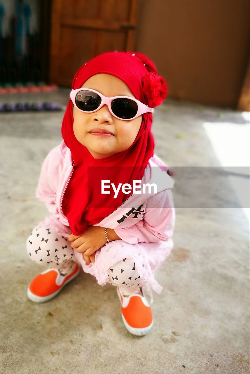 Full length of girl wearing sunglasses with hijab while crouching on floor