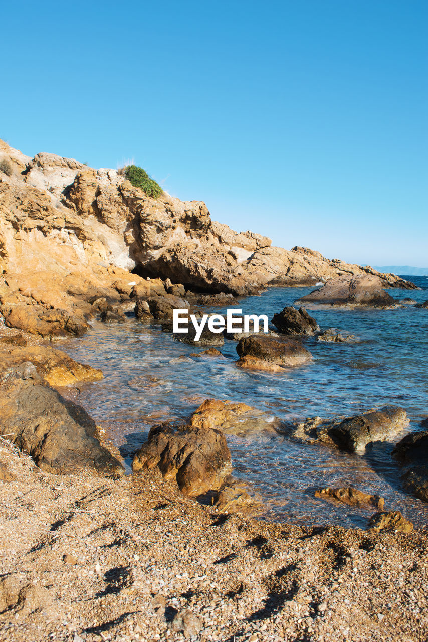 Rock formations in sea against clear blue sky