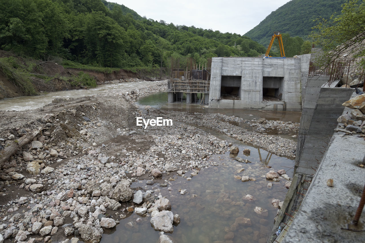 BUILT STRUCTURE BY RIVER AGAINST MOUNTAIN