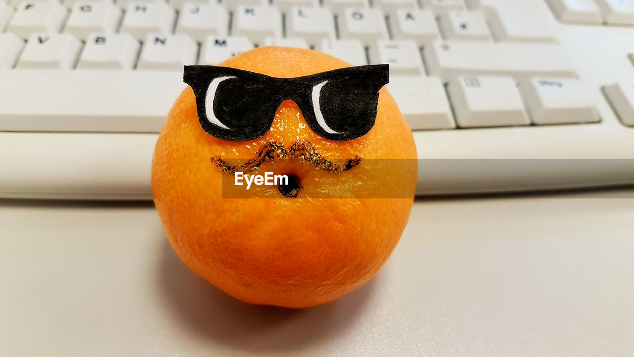 Close-up of orange with anthromorphic face on desk with computer keyboard