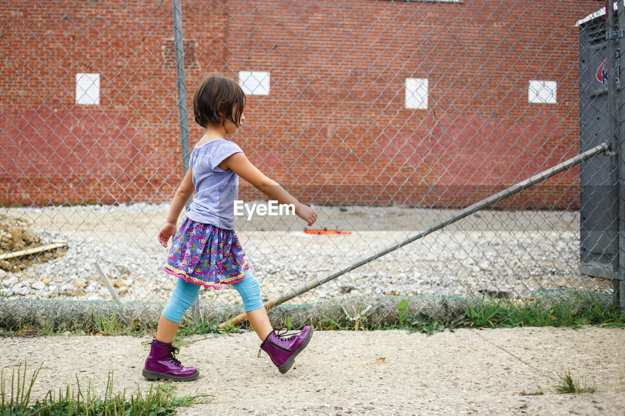 A bold girl in purple boots walks on sidewalk by a construction site