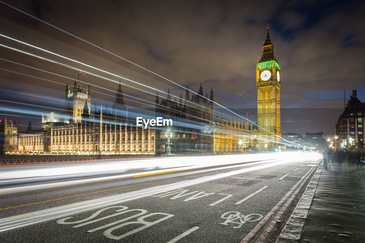 Light trails on road by big ben against sky in city at night