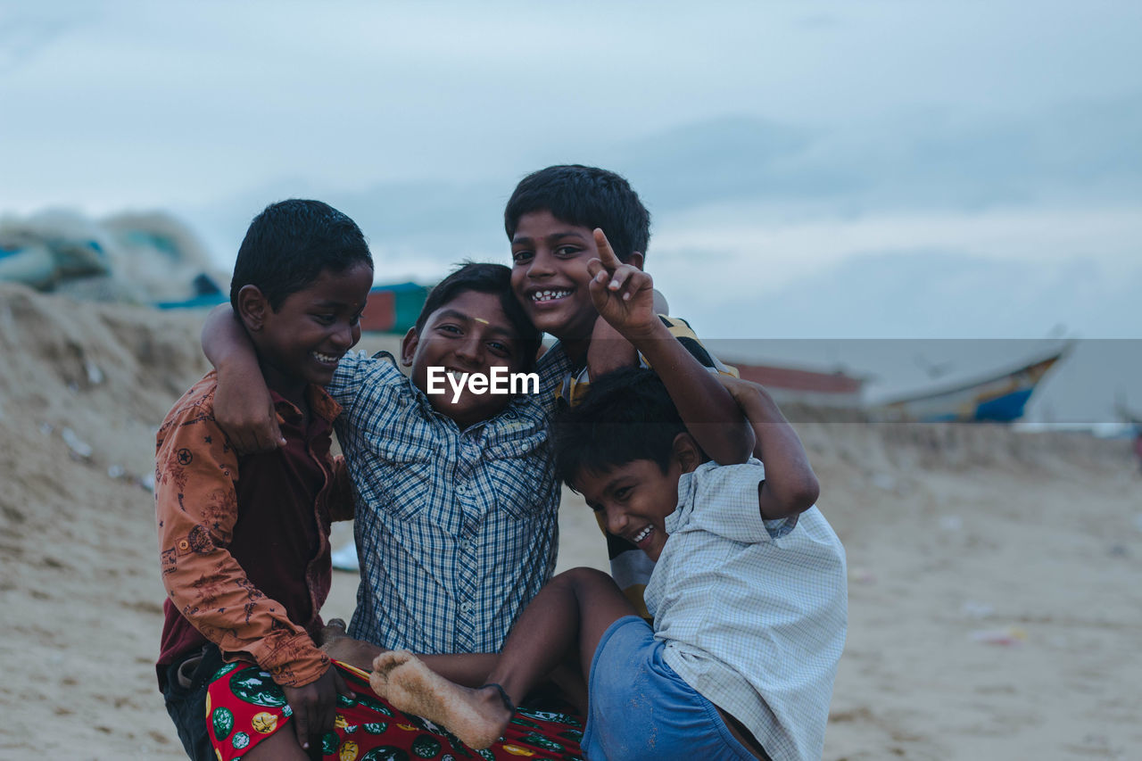 Portrait of boys playing at beach against sky