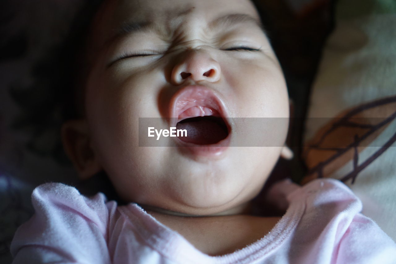 Close-up of cute baby girl with open mouth on bed