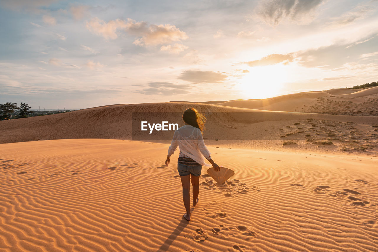 Rear view full length of man walking at desert during sunset