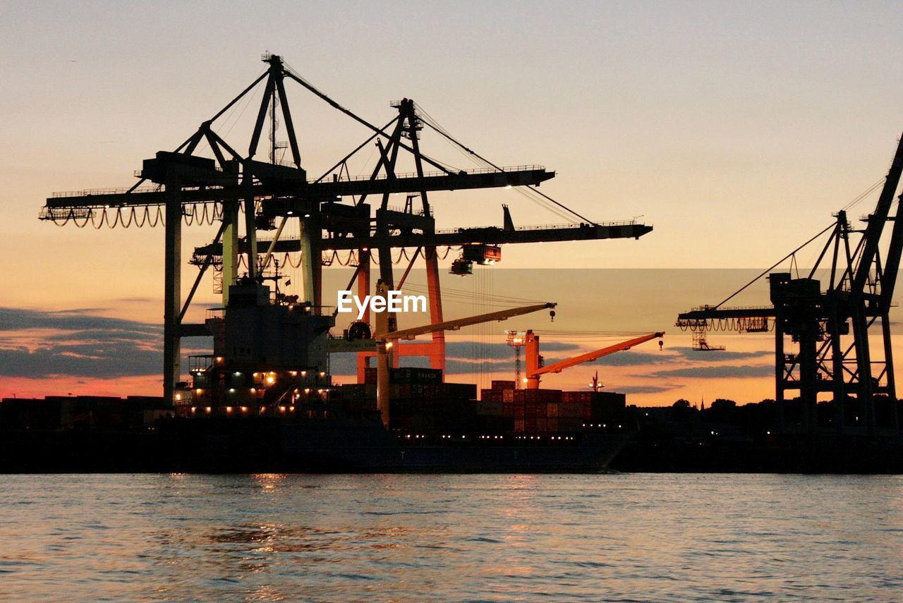 Silhouette cranes at harbor against clear sky