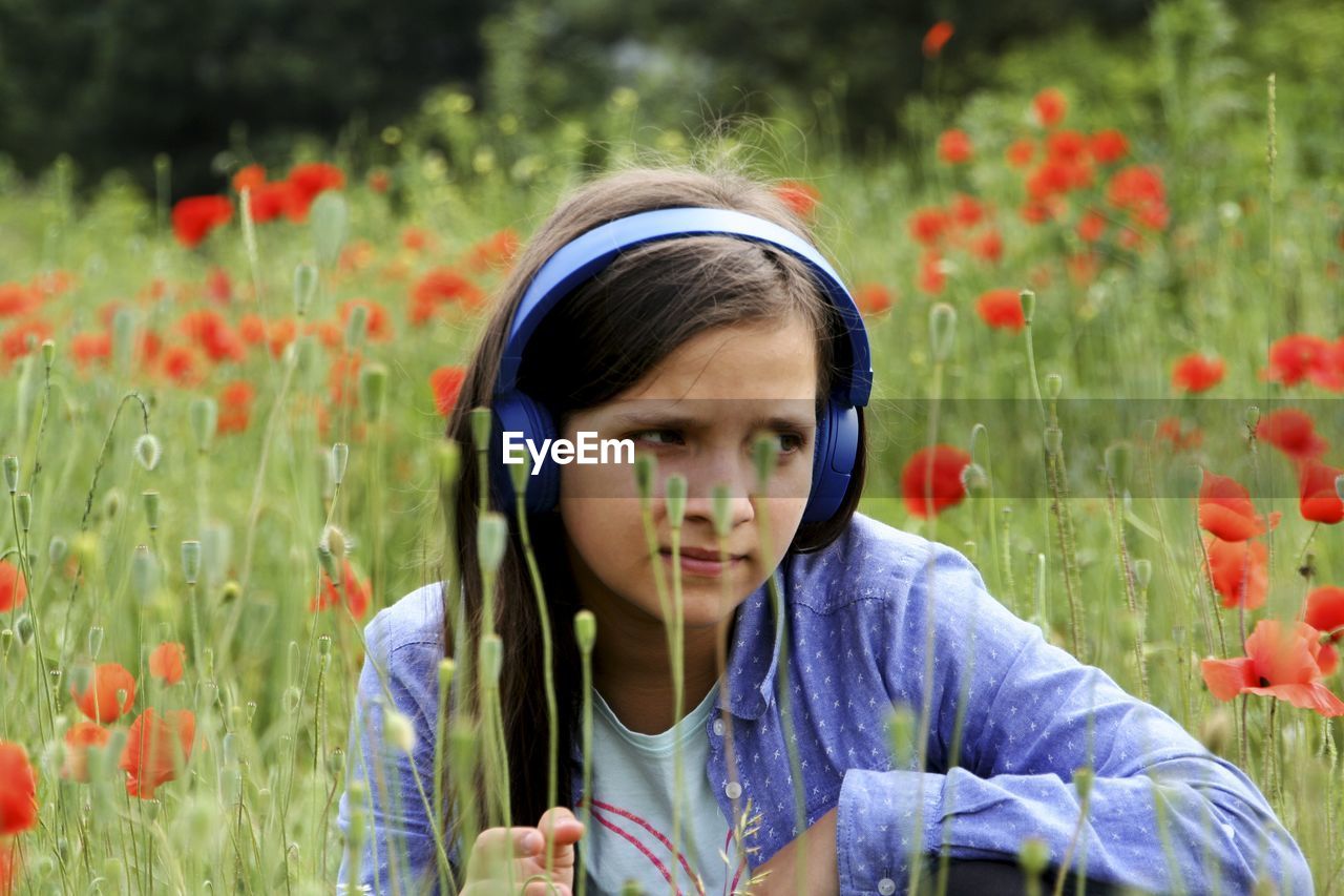 Girl listening music on field with red flowers