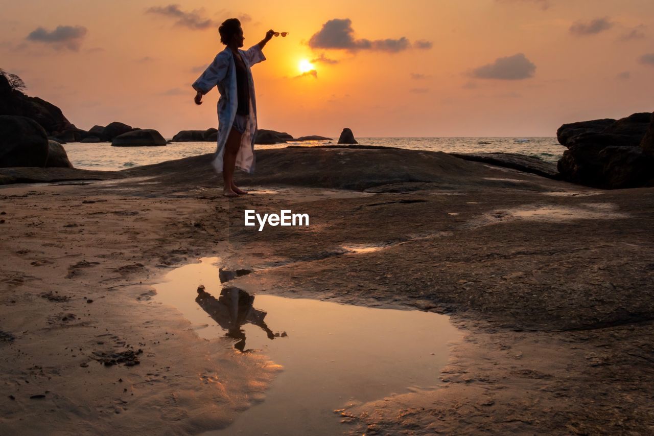 Woman standing at beach against cloudy sky during sunset