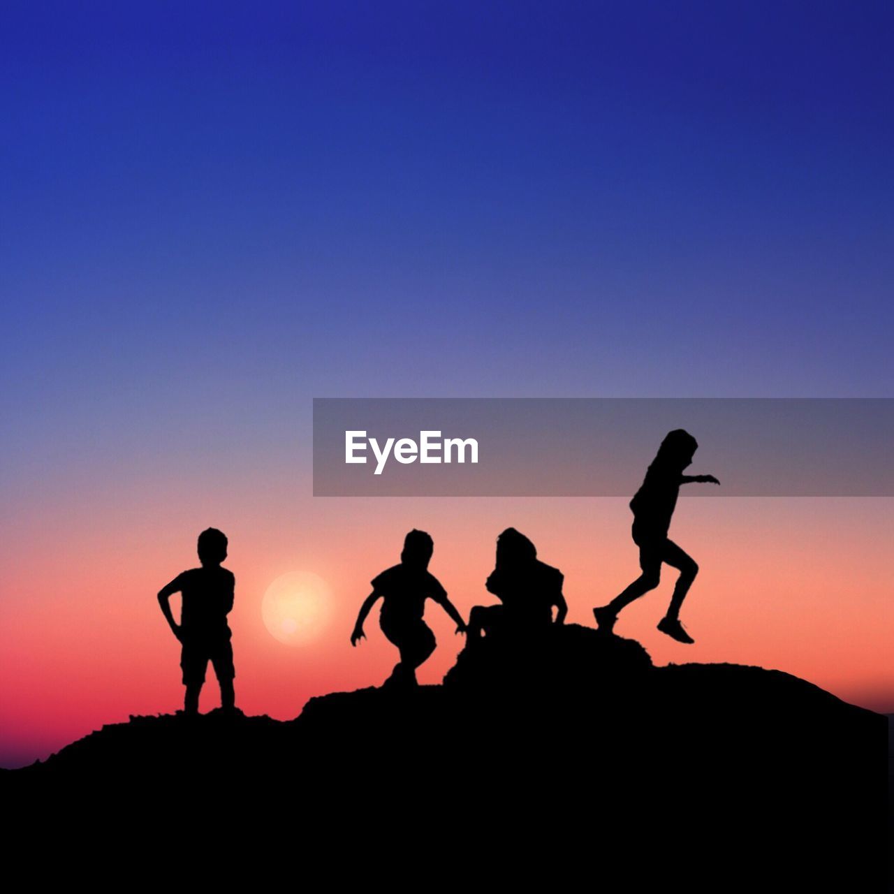 Silhouette children playing on rock against blue sky during sunset