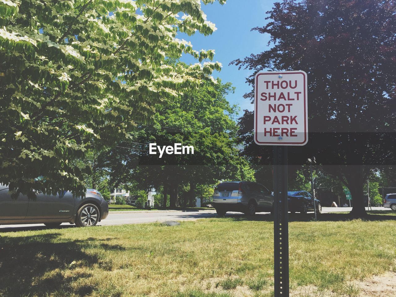 Warning sign on grassy field against parked cars by trees