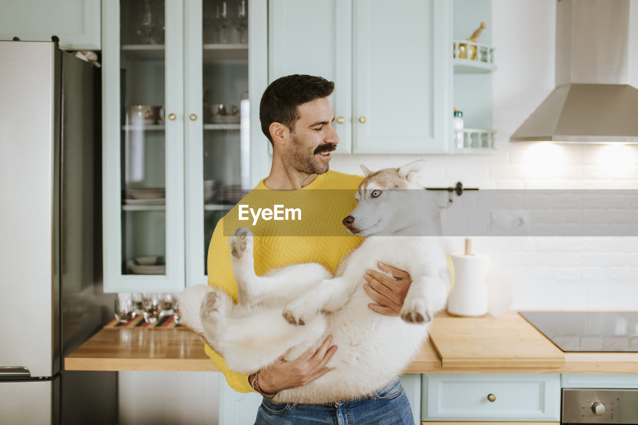 Man holding siberian husky in kitchen at home