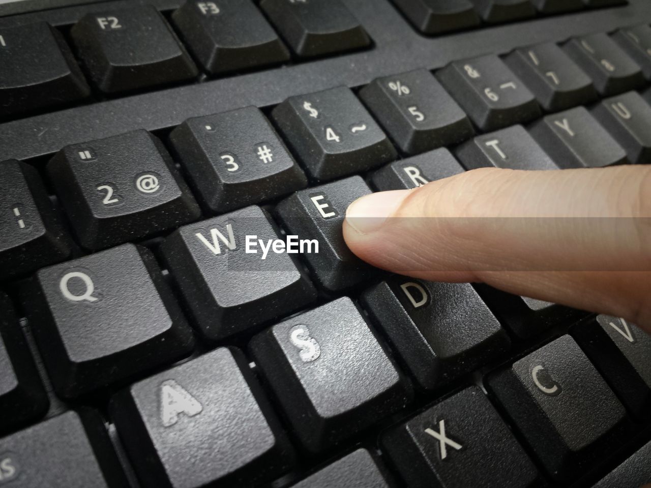Cropped hand of person typing letter e on keyboard