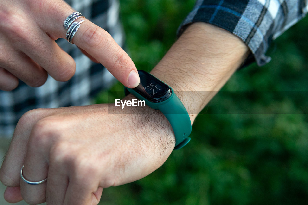 Closeup of crop anonymous male in casual checkered shirt touching smart watch and checking notifications