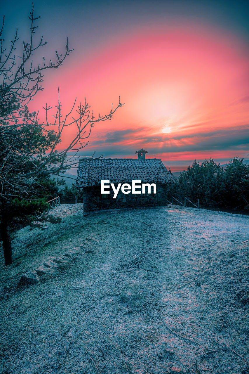 SCENIC VIEW OF BUILDING AND TREES AGAINST SKY AT SUNSET