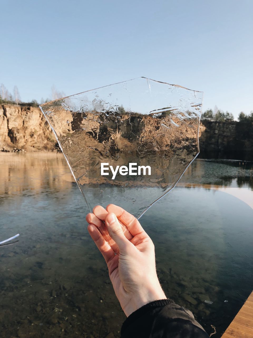 Close-up of hand holding ice against lake