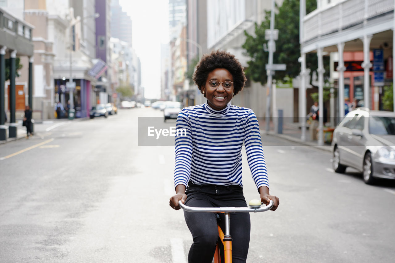 PORTRAIT OF SMILING YOUNG MAN RIDING BICYCLE ON CITY