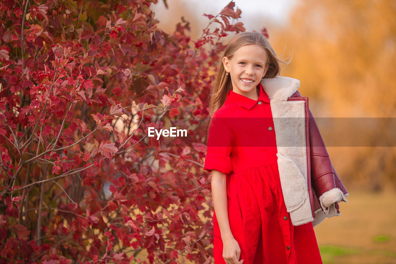 PORTRAIT OF A SMILING GIRL STANDING AGAINST TREES