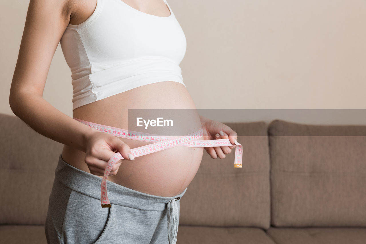 Midsection of woman measuring abdomen with tape measure