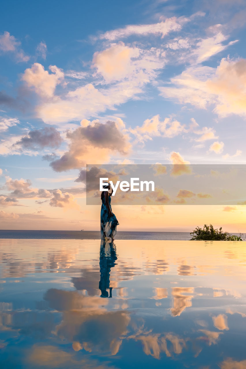 rear view of silhouette woman standing at beach against sky during sunset