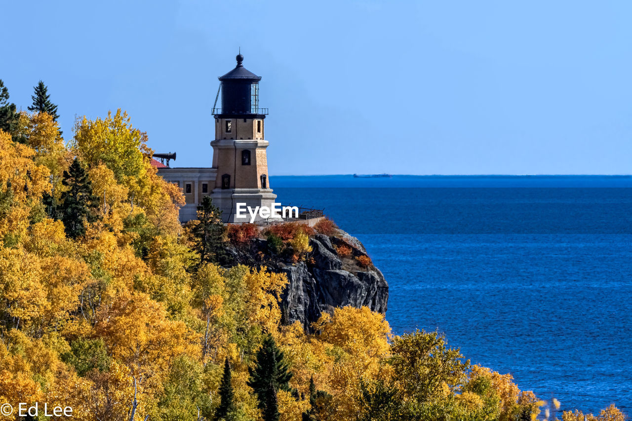 Lighthouse amidst trees and sea against sky