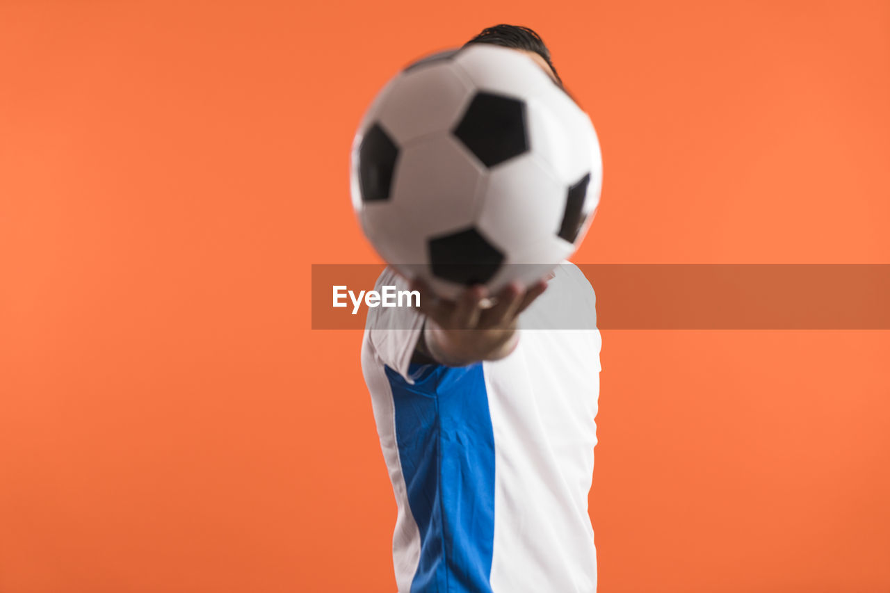 low section of woman holding soccer ball against yellow background