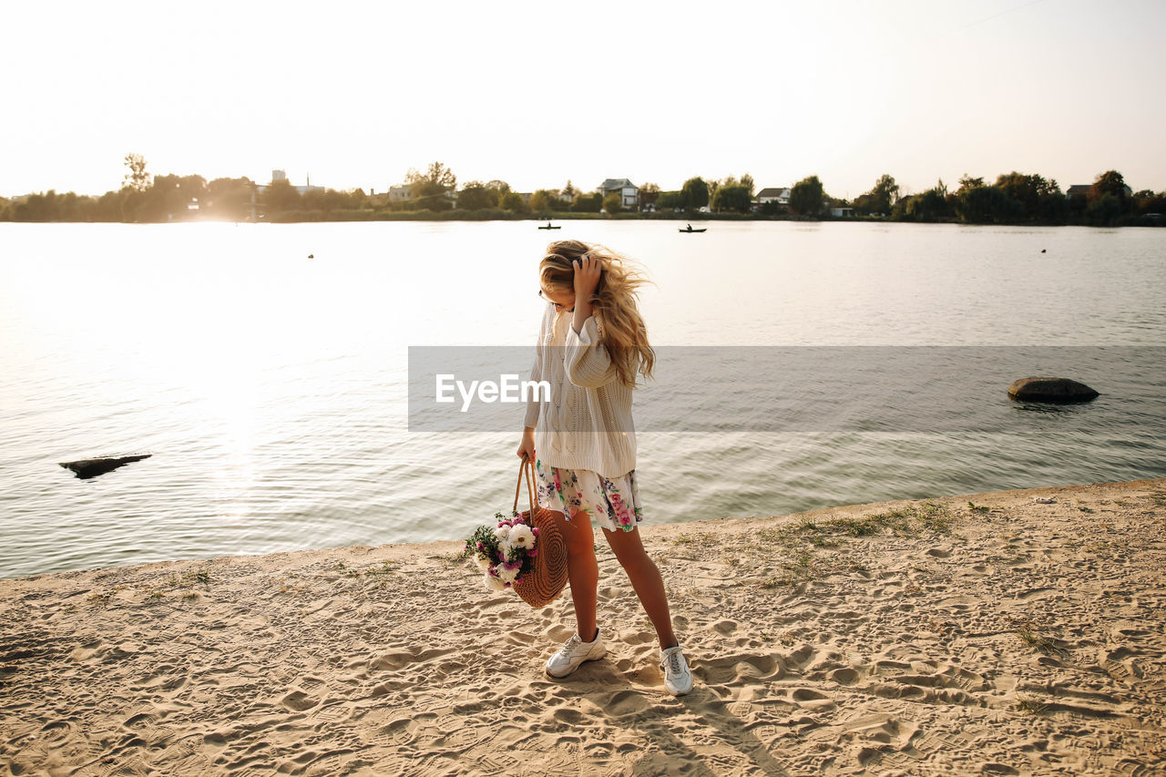 REAR VIEW OF PERSON STANDING AT BEACH AGAINST SKY