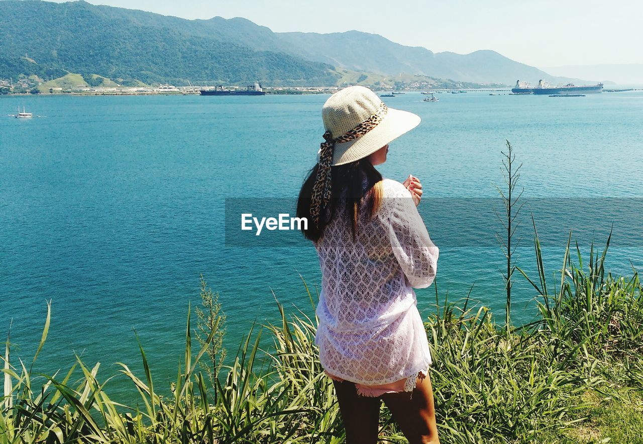 Rear view of woman wearing hat while standing by sea on sunny day