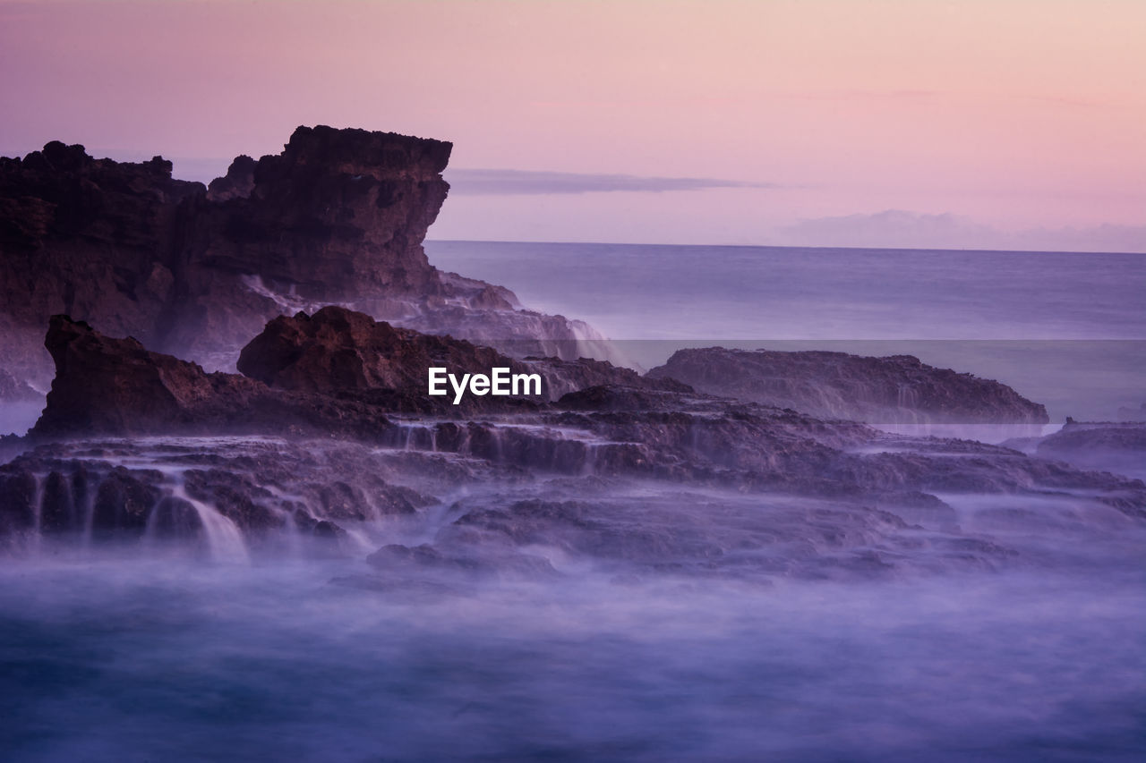 Rock formation in sea against sky during sunset