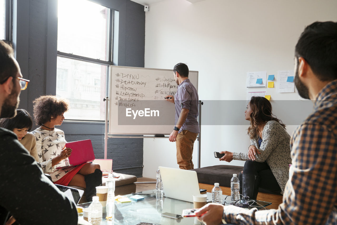 Colleagues looking at businessman writing on whiteboard in meeting