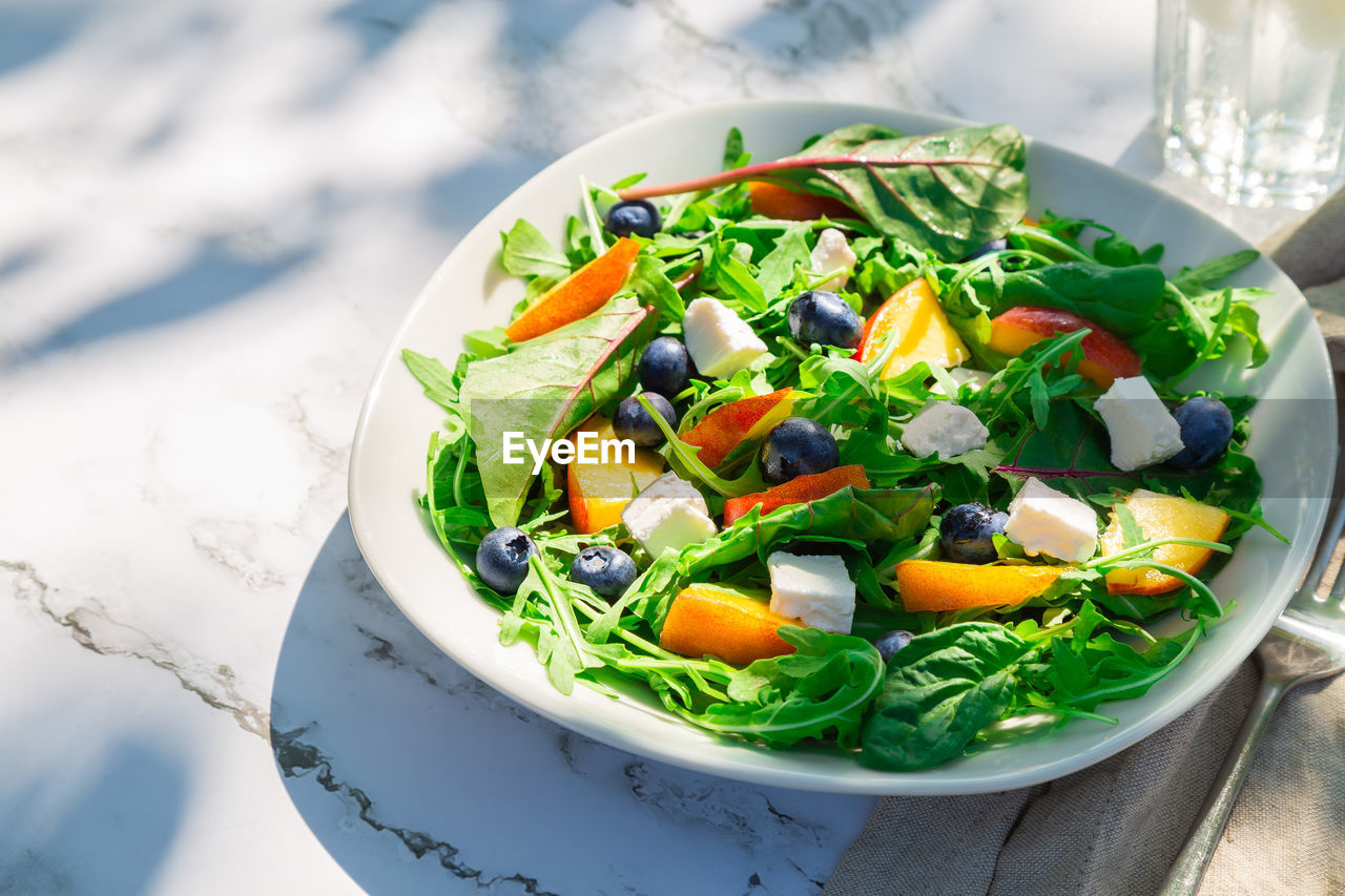 Salad with nectarines, blueberries, arugula, spinach and feta cheese on white marble background 