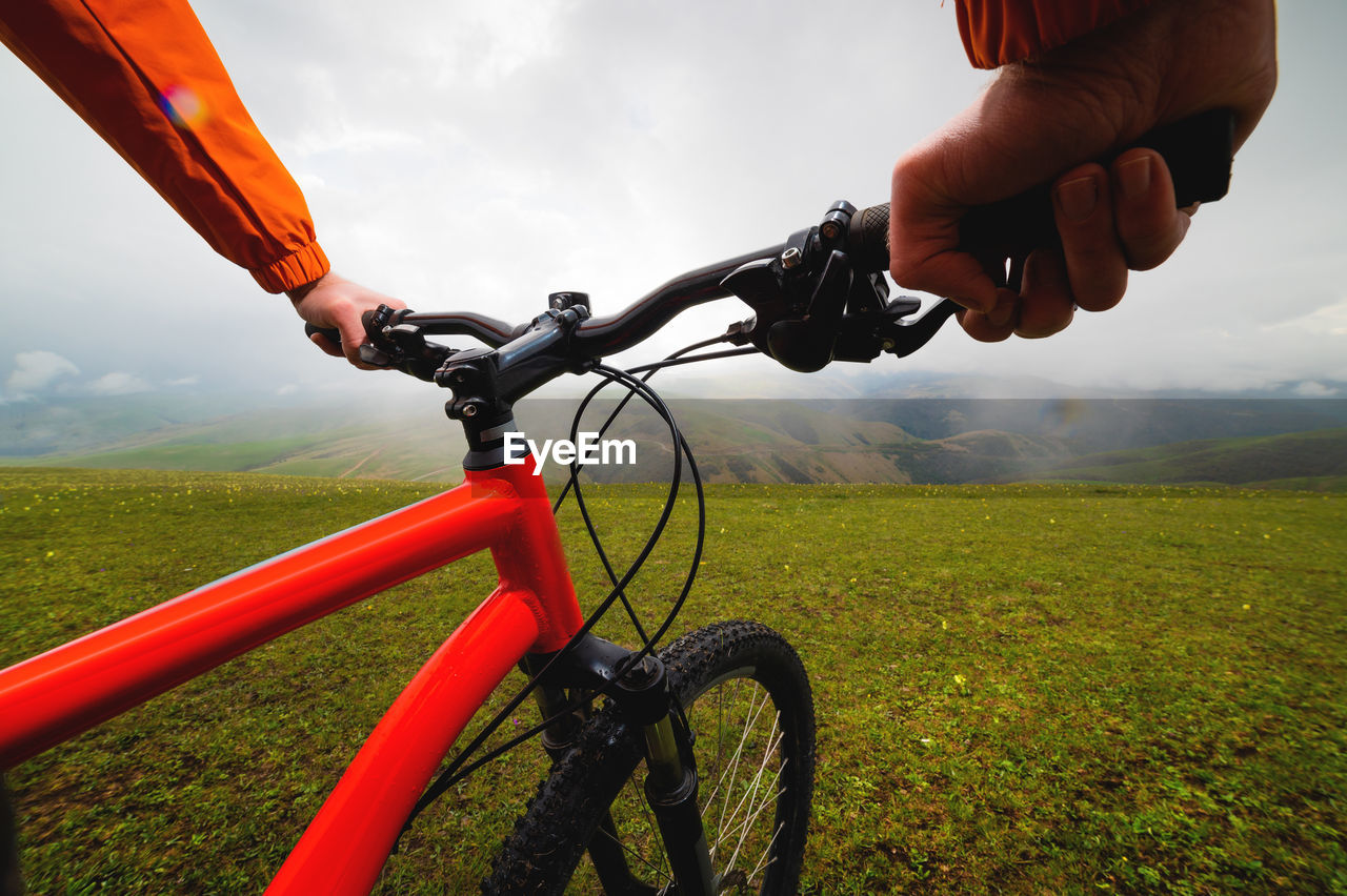 Hands hold the steering wheel of a bicycle while standing on a green meadow. a look through the eyes