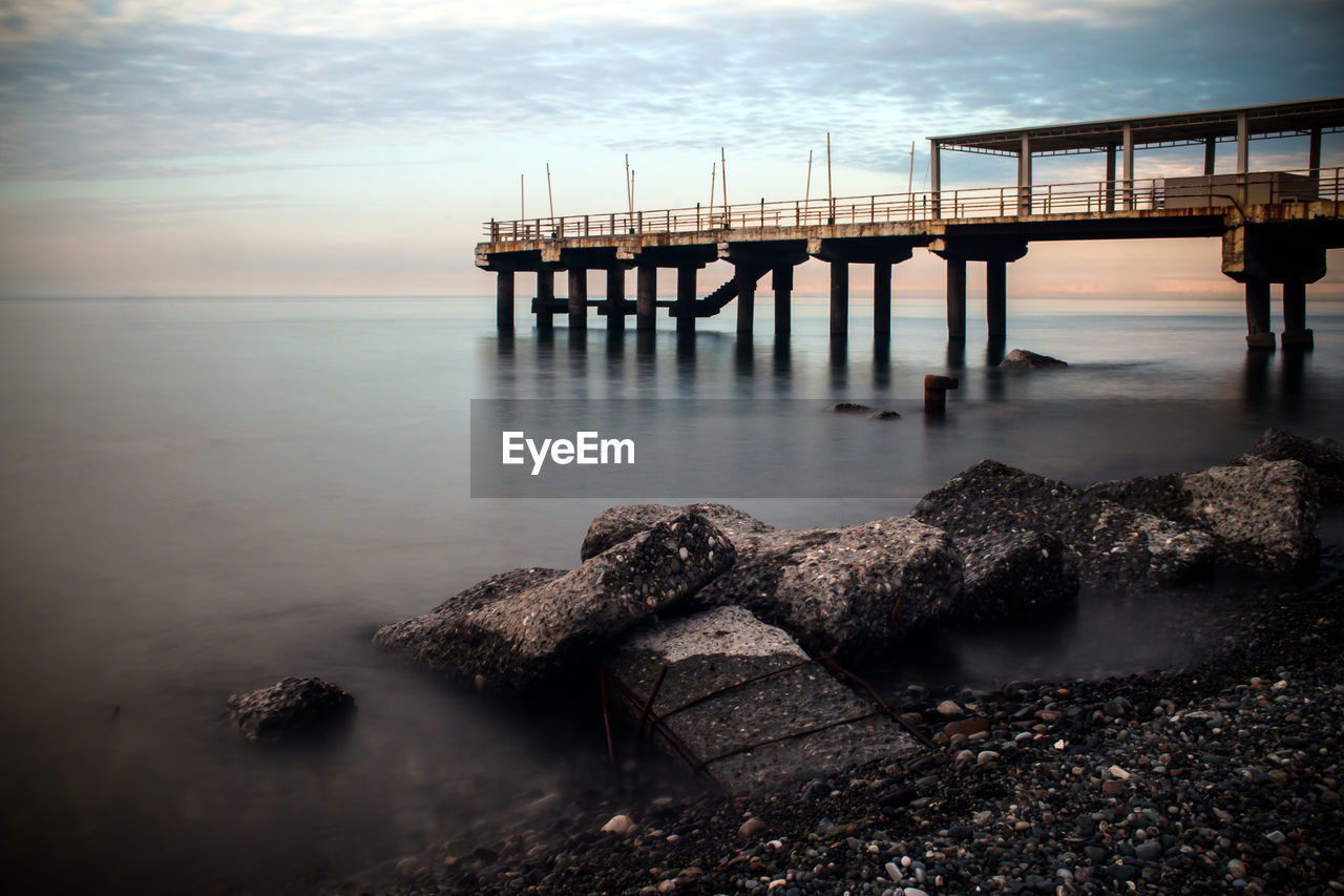 Low angle view of pier over river against sky during sunset