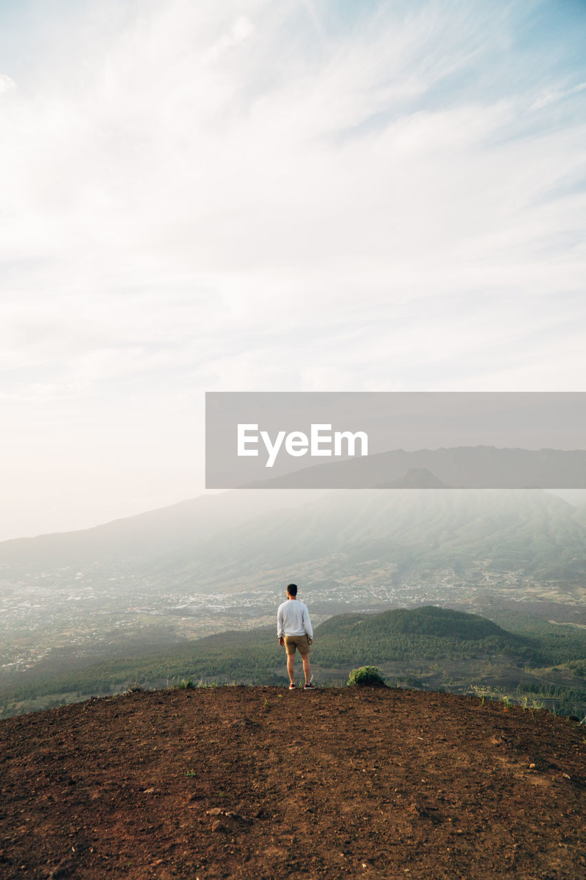 Rear view of man standing on mountain against sky