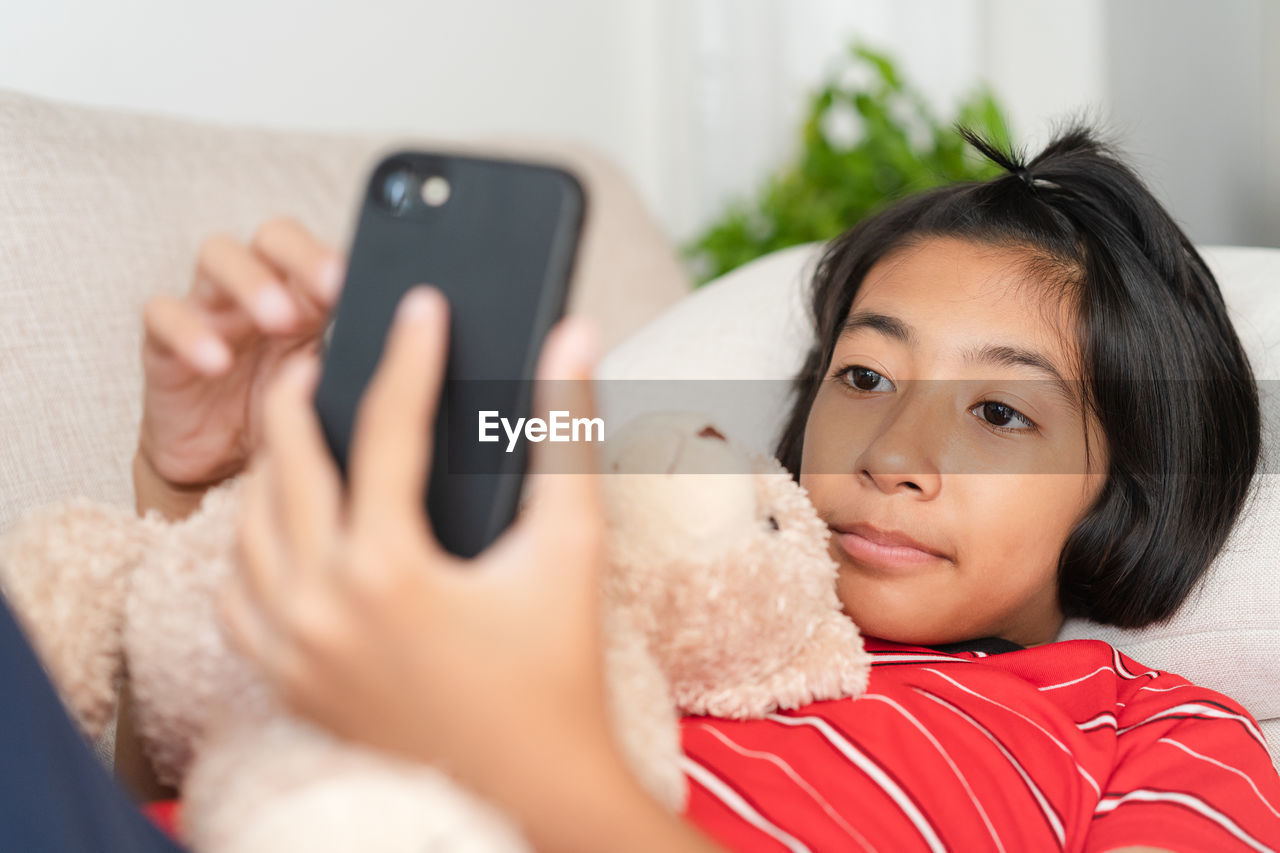 Close-up of girl using phone while lying on sofa at home