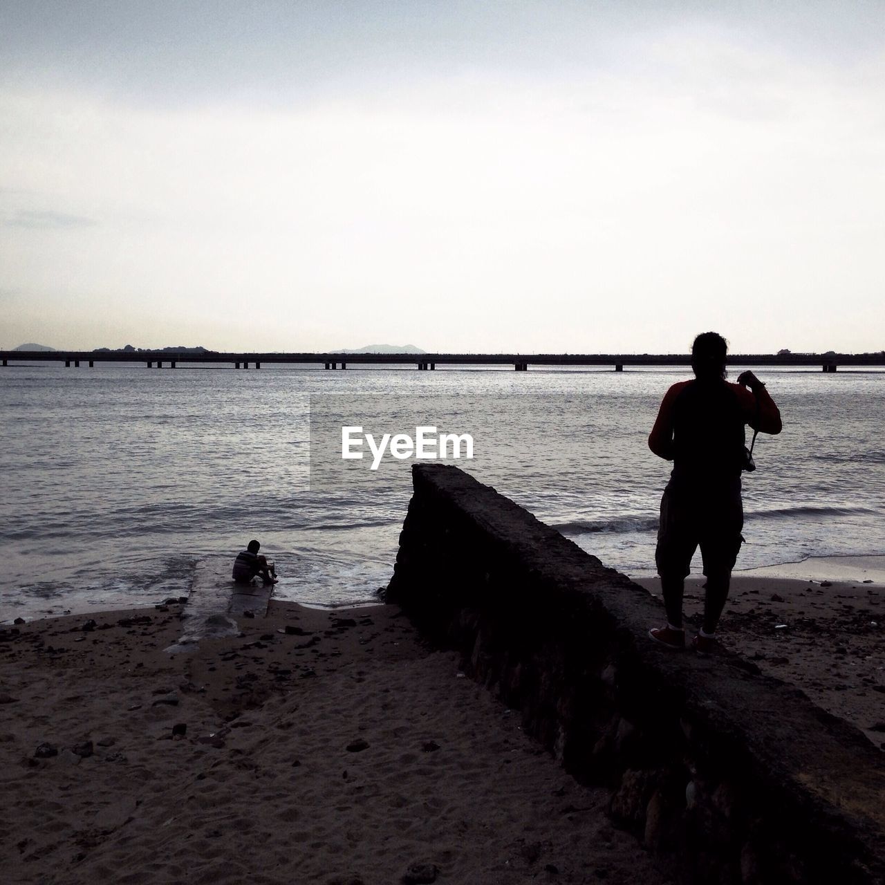 Rear view of man looking at view of sea while standing on wall against sky