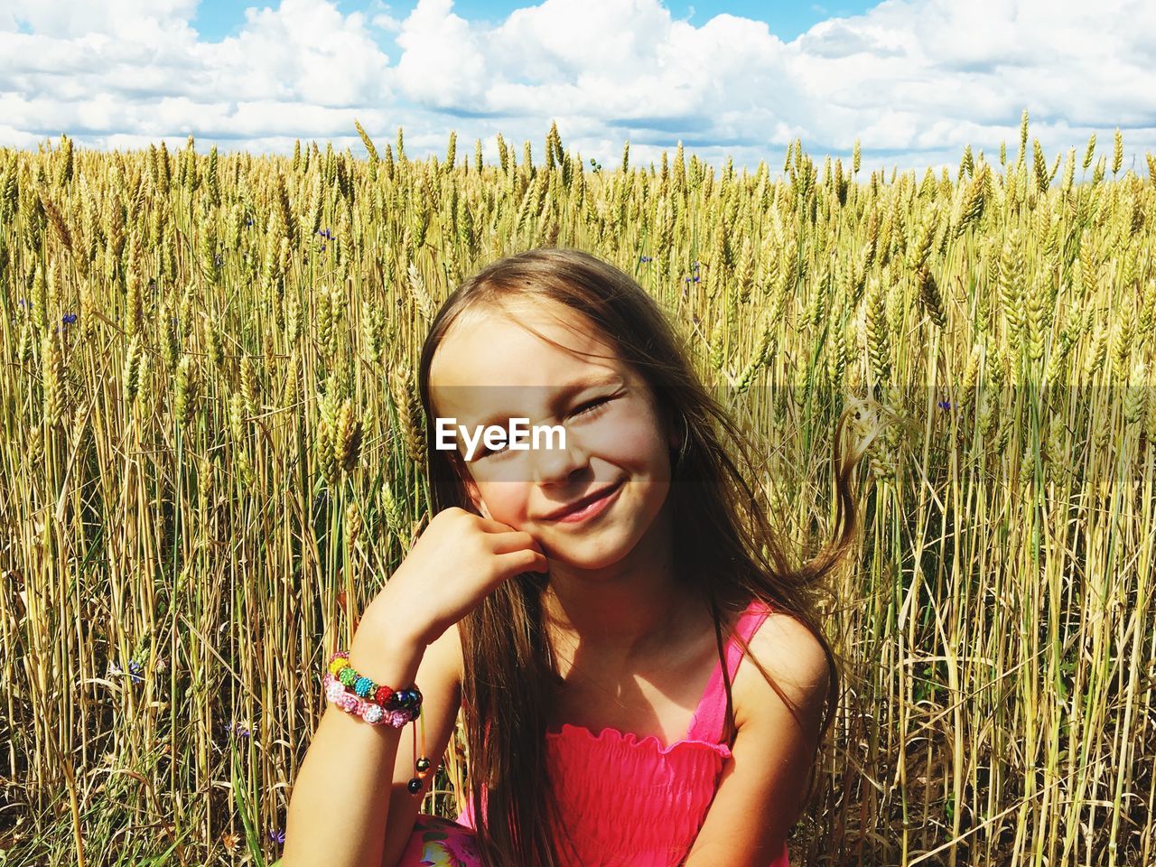 Cute smiling girl on agricultural field against crops