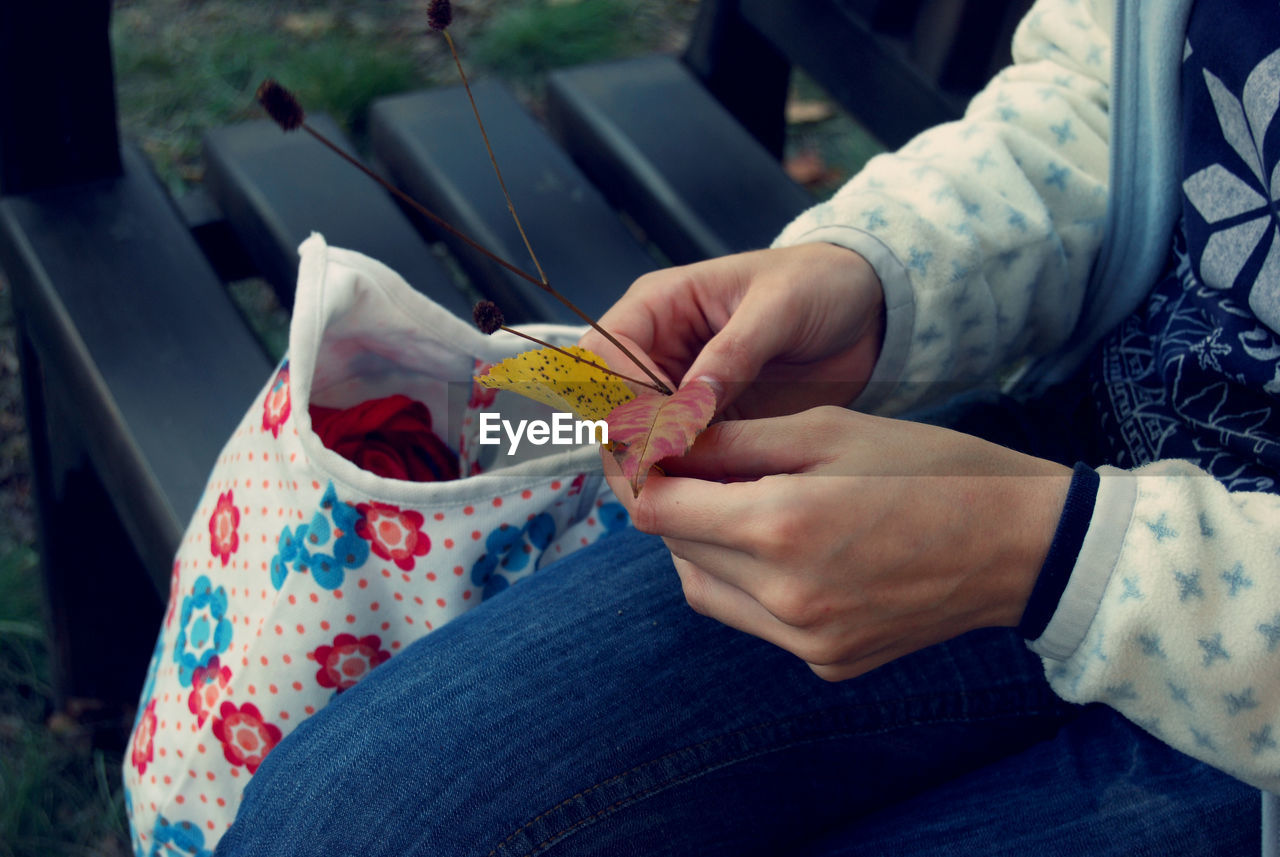 Midsection of woman holding leaves while sitting on bench