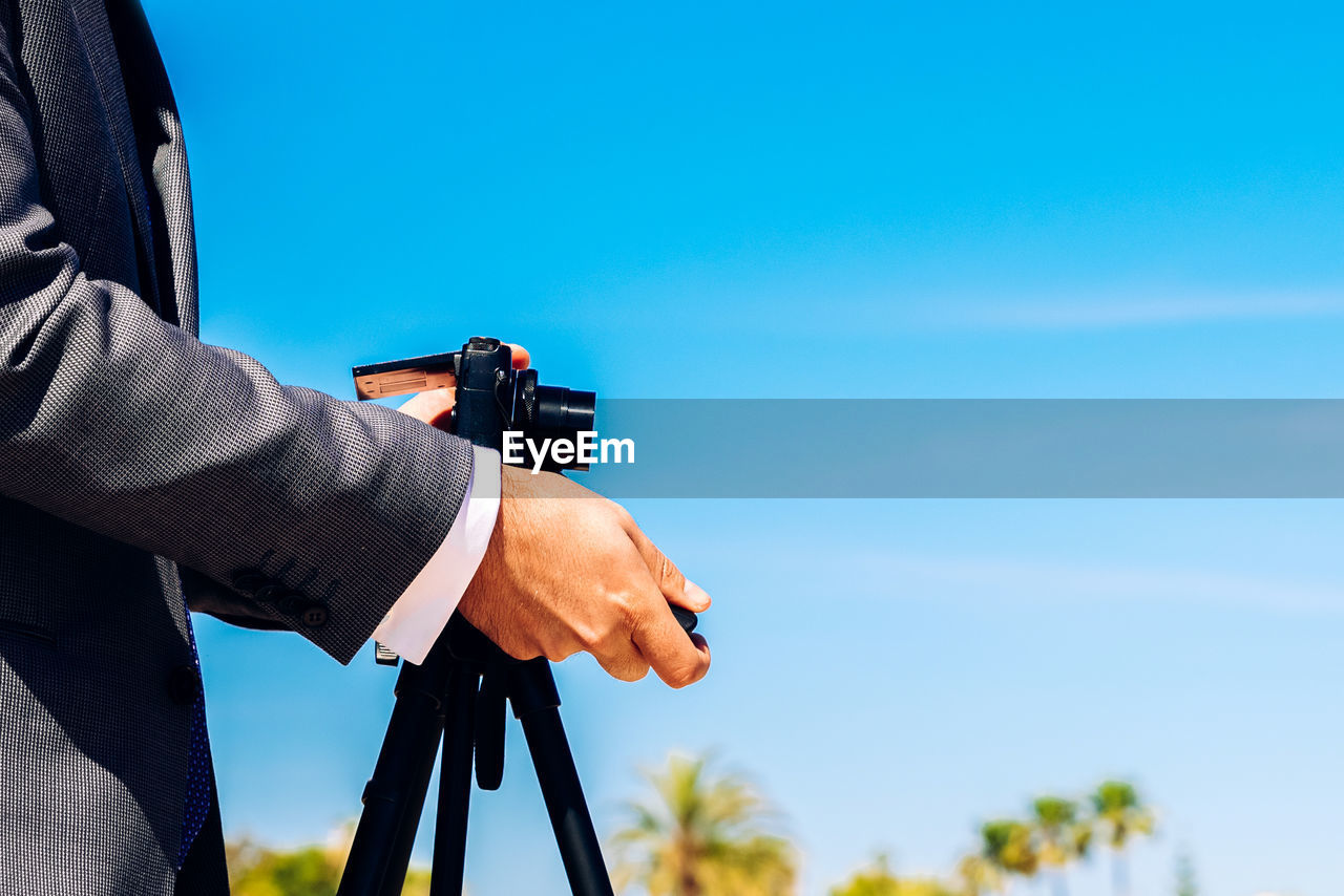 Midsection of man photographing while standing against blue sky