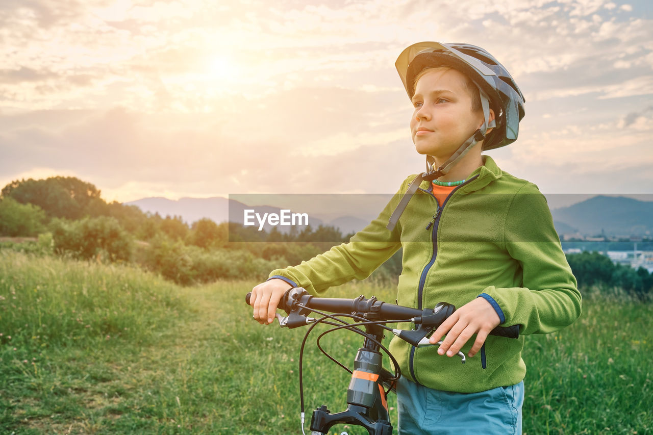 Happy boy in helmet to ride bicycle. learn to riding bike on green meadow in summer  at sunset time.