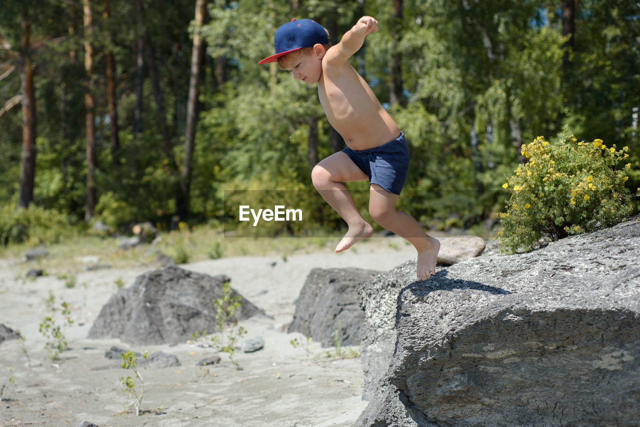 Full length of shirtless boy on jumping on rock