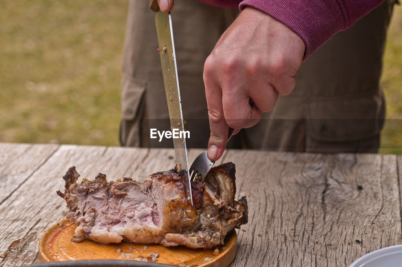 Close-up of hands using fork and knife to eat meat