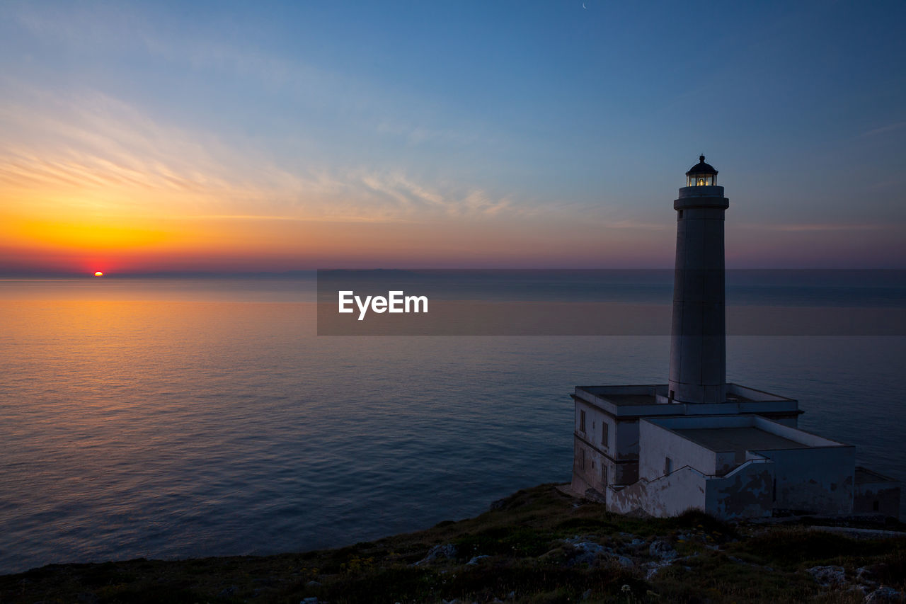 Lighthouse by sea against sky at dawn