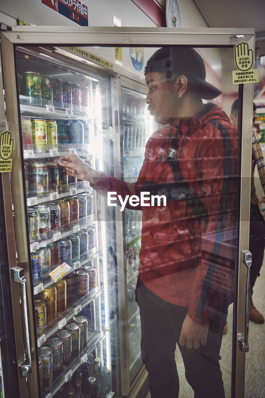 SIDE VIEW OF YOUNG MAN STANDING BY GLASS STORE