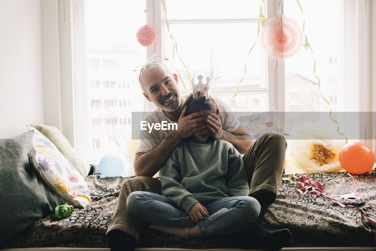 Portrait of happy man covering daughter's eyes during birthday celebration at home