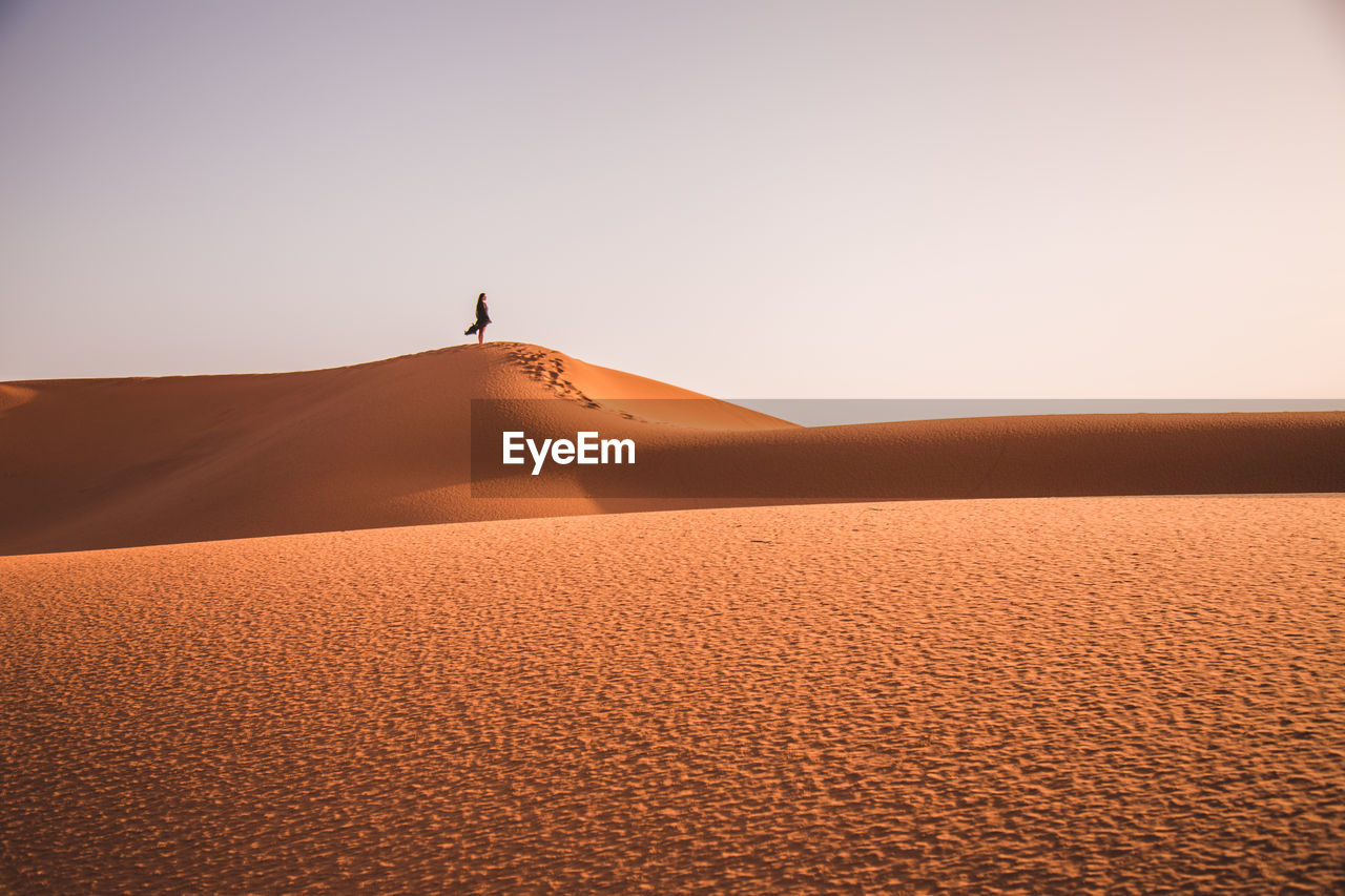 Full length of woman standing on sand dune in desert against sky